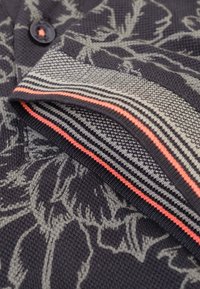  gebreide cardigan in donker marineblauw met een grijs bloemenpatroon. Heeft een gestreepte kraag met rode, grijze en zwarte accenten. Knopdetail zichtbaar.