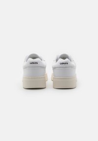 Białe skórzane trampki z jasnobeżową gumową podeszwą i subtelnymi przeszyciami. Logo "LEVI'S" nadrukowane na tylnej pięcie. Czysty, elegancki design.