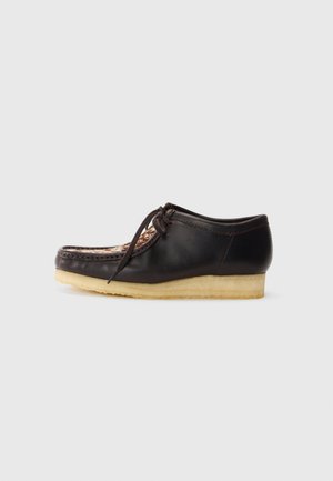 Brown leather shoe with a rounded toe, decorative stitching, lace closure, and a light-colored rubber sole. Features a textured insole.