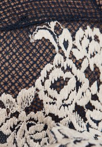 Marinblå spets tyg med ett intrikat blommönster i krämfärg, med fin nätdetalj och strukturerad broderi genom hela.