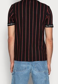 Czarna koszulka z krótkim rękawem w czerwone pionowe paski. Posiada okrągły dekolt oraz detal tekstowy na rękawie. Wykonana z bawełny o gładkiej fakturze.