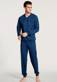 Ensemble de pyjama en coton bleu marine composé d'un haut à manches longues en V avec de petits pois blancs et d'un pantalon assorti à taille élastique avec des jambes fuselées.