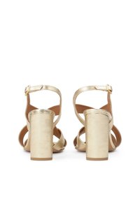 Gouden sandalen met hakken en een metallic afwerking, voorzien van een blokhak, enkelbandjes en een kruislings bovenwerk. Glad textuur, minimalistische stijl.
