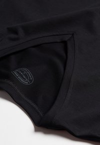 Svart kortärmad skjorta med V-ringning, som har en mjuk tygtextur och en liten tryckt etikett i nederkant. Kanterna har synlig sömnad.