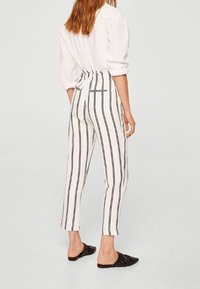 Pantaloni a vita alta a righe in bianco e nero, caratterizzati da un design a gamba affusolata, tasche posteriori e un tessuto testurizzato.