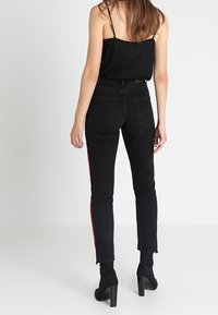 Černé džíny z denimu s červenými bočními pruhy, vysokým pasem, rovné nohavice, zadní kapsy, doplněné černými botami na podpatku do kotníku.