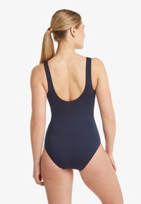 Marineblauwe badpak met een ronde rug. Het heeft brede schouderbanden en een naadloze textuur, vervaardigd uit stretchy materiaal.