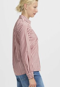 Camicia a maniche lunghe a righe rosse e bianche con colletto, polsini con bottoni e vestibilità comoda, abbinata a jeans in denim blu.