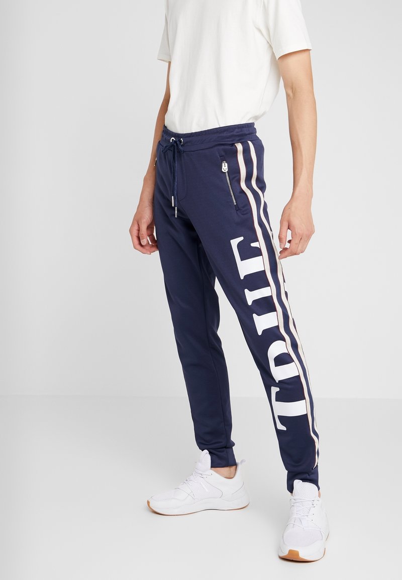 Marinblå sweatpants i mjukt material med sidosträck och stor "TRUE"-text. Har en elastisk midja med dragsko och fickor med dragkedja.