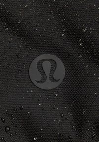 Schwarzer Stoff mit einer gestrickten Textur, der Wassertropfen zeigt, und einem auffälligen schwarzen Logo in der Mitte, das ein schlankes Design vermittelt.