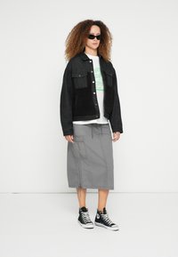 Fekete farmerdzseki műszőrmével az elején, szürke cargo szoknya húzózsinórokkal, és fekete magas szárú tornacipő. A modell sötét napszemüveget visel.