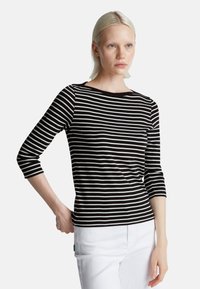 Czarna i biała pasowa bluzka z długim rękawem, z dekoltem w łódkę i rękawami o długości trzy czwarte, wykonana z miękkiego materiału. Połączona z białymi spodniami.