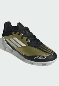 Botín de fútbol negro y dorado con un upper texturizado, cordones negros y detalles blancos. Presenta un diseño puntiagudo y tachuelas redondas y transparentes.