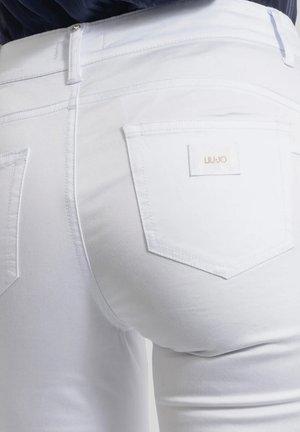 Primo piano di una persona che indossa jeans bianchi aderenti con tasche posteriori, con una piccola etichetta sulla tasca destra con la scritta "LIU JO."
