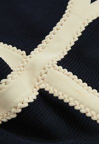 Námornícky textúrovaný materiál s krémovými opletenými akcentmi a pruhmi, s krížovým vzorom a vertikálnym vrúbkovaním pre zvýraznenie rozmerov.