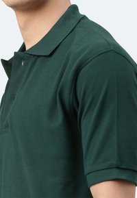 Polo shirt verde scuro realizzato in cotone tessuto, con colletto, pattina con tre bottoni e maniche corte con silhouette aderente.