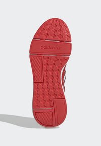 Röd yttersula med strukturerat grepp, tre vita ränder och Adidas-logotyp. Släta kanter och cirkulära mönster förbättrar grepp och design.