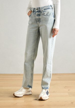 Jeans alta vita di colore azzurro chiaro con una vestibilità rilassata, dotati di cinque tasche e un leggero sbiadimento. Un basic bianco a maniche lunghe è indossato sopra.