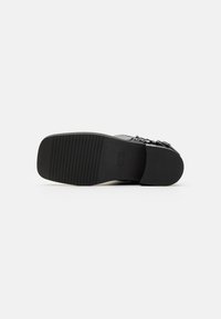 Semelle de chaussure noire à texture striée, dotée d'un design plat et de peu de quincaillerie. Surface lisse avec une finition globale épurée.