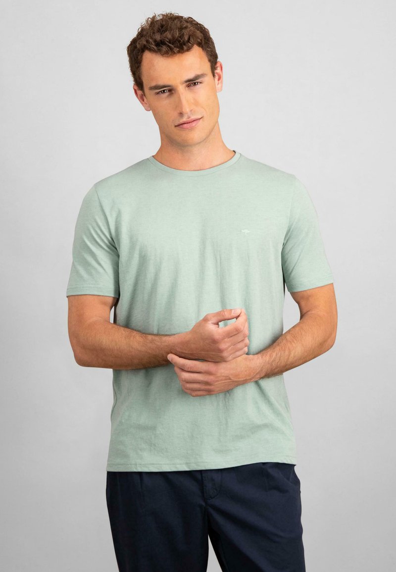 Mint green cotton t-shirt with short sleeves and a round neckline. Features a subtle logo detail on the chest. Paired with dark shorts.