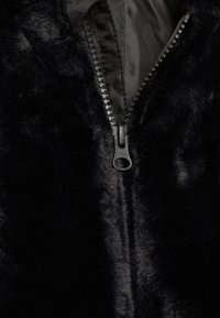 Zwarte nepbontjas met een gladde binnenvoering, ritssluiting met YKK-hardware en een zachte, pluizige textuur.