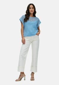 Top de malla azul claro con un corte relajado, combinado con pantalones anchos blancos y sandalias de tacón ligero en color beige.