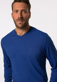 Camiseta de manga larga azul con escote en V, hecha de material ligero. Cuenta con un bolsillo en el pecho izquierdo con detalle de logotipo en relieve.