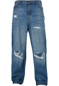 Kopott kék denim farmernadrág laza szabással, több elhasználódott folttal és rojtos szélekkel. Megerősített zsebek és gombos záródás.