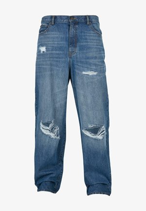 Tükkün sinised denim püksid, millel on lahtine lõige, mitme kulunud pleki ja hargnenud servadega. Tugevdatud taskud ja nööbiga sulgemine.