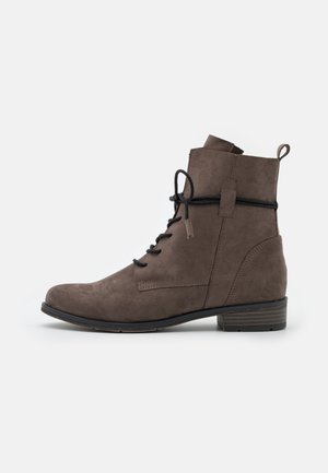 Bottine en suède marron avec lacets noirs, petit talon empilé, languette de tirage et détails de couture latéraux sur fond blanc.