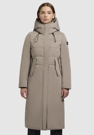 Manteau long beige avec un corps rembourré, capuche ajustée, fermeture éclair à l'avant et deux poches latérales. Caractérisé par un tissu texturé et des cordons de serrage réglables.