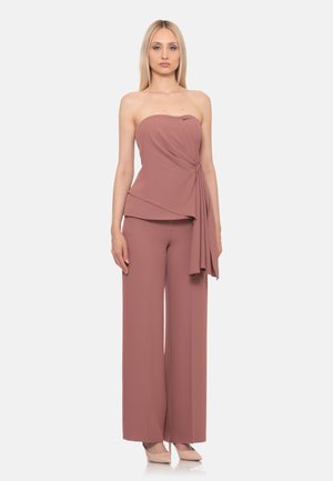 Donna che indossa un top senza spalline color malva con dettaglio drappeggiato e pantaloni larghi abbinati, in piedi davanti a uno sfondo chiaro e semplice.