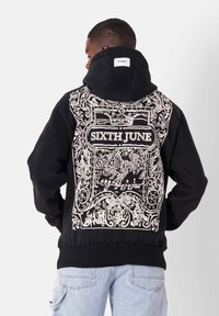 Sudadera negra con una gran gráfica blanca en la parte posterior, que presenta diseños ornamentales y el texto "SIXTH JUNE". Tejido grueso y capucha amplia.