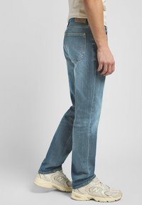 Light blue denim jeans with a slim fit, five-pocket design, and contrast stitching. Worn with beige athletic shoes.