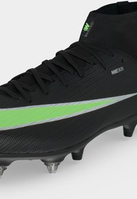 Μαύρο ποδοσφαιρικό παπούτσι Nike με πράσινο και ασημί λογότυπο, μαύρα κορδόνια, ψηλό κολάρο στον αστράγαλο και μεταλλικά καρφιά στη σόλα.