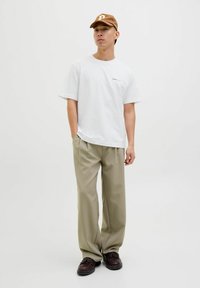 Bílá oversized tričko s jemným logem, kombinované s khaki širokými kalhotami a tmavě hnědými botami. Hnědá kšiltovka s detailním logem.