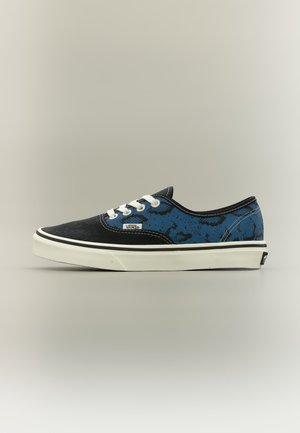 Baskets basses Vans avec bout noir, côté à motifs bleu et noir, lacets blancs et semelle blanche avec bande noire.
