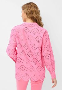 Camicetta rosa a maniche lunghe con delicati ritagli ad occhio in un design scallop. Tessuto morbido, con maniche a palloncino che terminano in polsini aderenti.