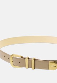 Ceinture en cuir beige clair avec une finition lisse. Elle possède une boucle et des détails en métal doré. Le nom de la marque "GUESS" est embossé sur les éléments métalliques.