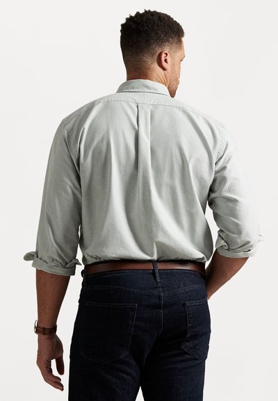 Šviesiai žalia medvilninė marškinėliai su užsuktais rankovėmis, matomi iš nugaros. Suderinti su tamsiai džinsiniais kelnais ir rudos odos diržu.