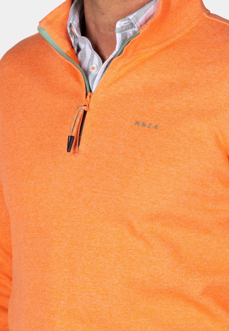 Pomarańczowy polar z półkolażowym zamkiem, z kontrastowym zielonym zamkiem i lekką teksturą. Wyszywane logo "NZLA" na klatce piersiowej.