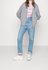 Sudadera gris con cremallera y cordones, camiseta de tie-dye en tonos pastel, jeans azul claro y zapatillas blancas con suela gruesa.