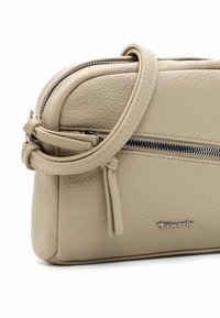 Borsa a tracolla in pelle beige con una texture liscia, chiusura con zip, tracolla regolabile e un piccolo logo sulla parte anteriore. Design compatto.