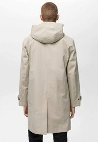 Parka impermeabile beige chiaro con cappuccio, caratterizzata da un taglio dritto, maniche lunghe e dettagli in bottone sui polsini. Texture liscia.