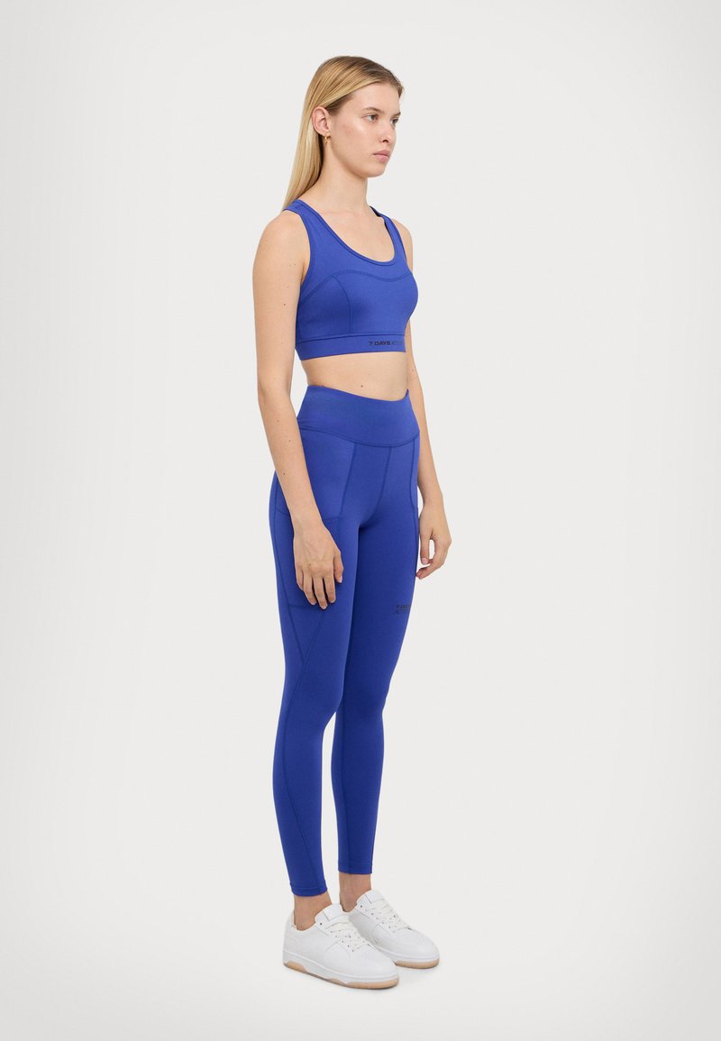 Blue athletic crop top and leggings made of stretch fabric. Top has a wide strap design; leggings feature a side pocket and high waistband.