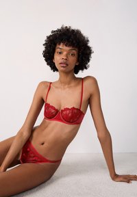 Rood lingerieset met doorzichtige kantcups met bloemenpatronen en dunne bandjes, gecombineerd met bijpassende bikini-stijl onderbroekjes. Soepele textuur.