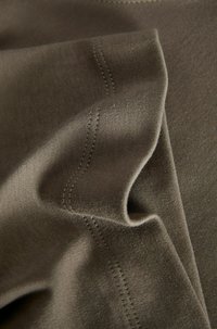 Brauner Baumwollstoff mit glatter Textur, der sichtbare Nähdetails und subtile Falten aufweist, in überlappenden Schichten angeordnet.