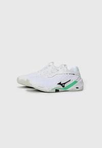 White sports shoes with textured fabric, black and green accents, a cushioned sole, and reinforced heel for stability.