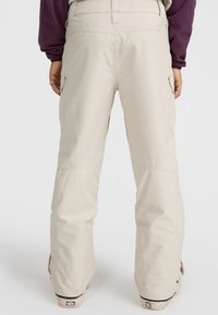 Beige snow pants with a relaxed fit, featuring large side pockets, adjustable waistband, and reinforced cuffs for durability.