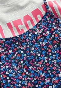 Graues T-Shirt mit pinkem "CALIFORNIA"-Text und Design von 1982, übereinander getragen mit einem marineblauen Blumenkleid mit bunten kleinen Blumen auf einem weichen Stoff.